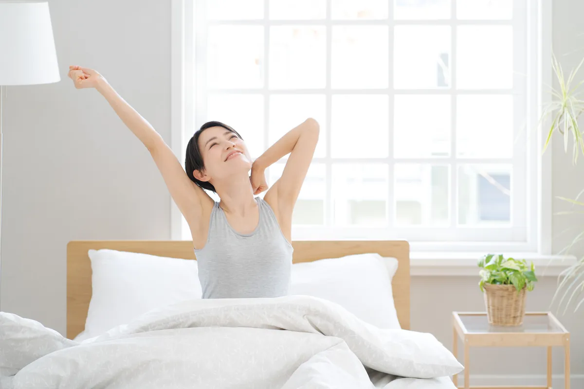 朝ベッドで伸びをする女性（イメージ）